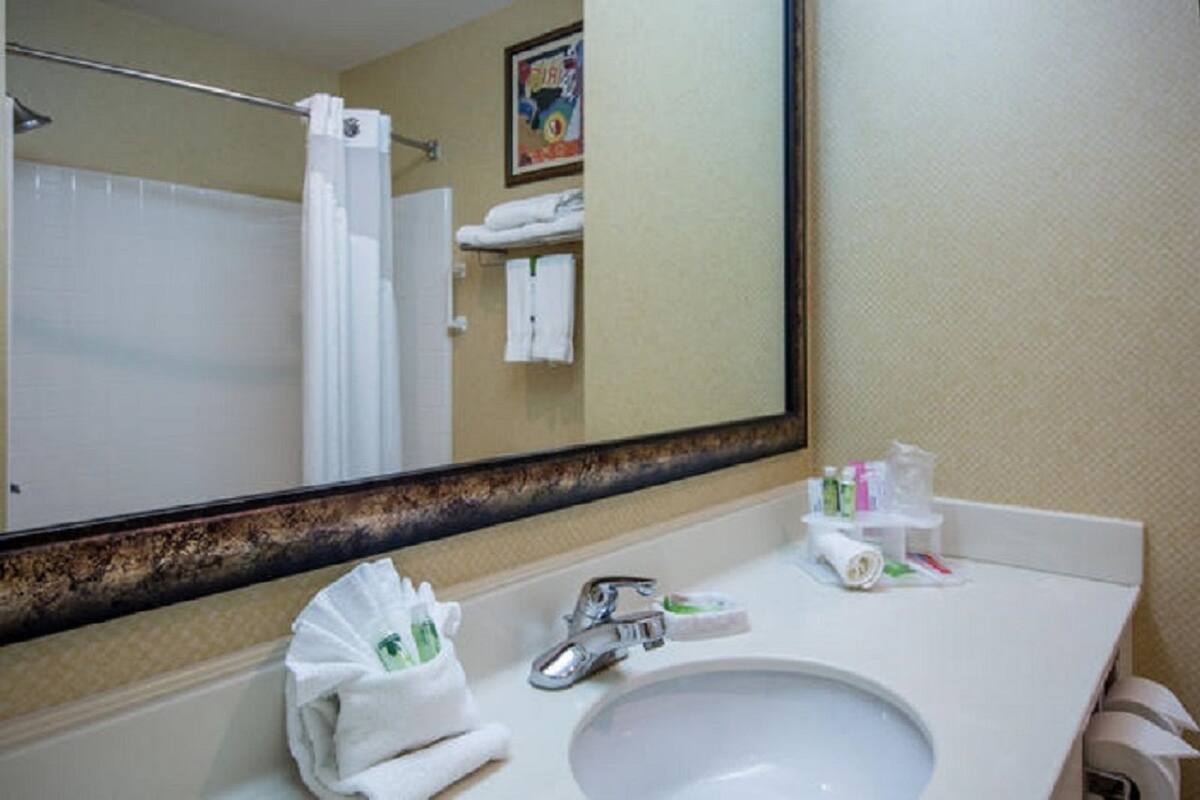 Ein Hotelbad mit einem großen Spiegel, einem Waschbecken und Pflegeprodukten auf der Ablagefläche.