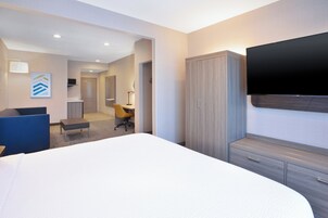 A hotel room with a large bed, a desk, a chair, a wardrobe, and a flat-screen TV.