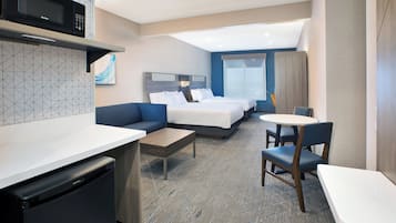 Ein Hotelzimmer mit Küchenzeile, einer Couch, einem Bett, einem Esstisch und einem Stuhl.