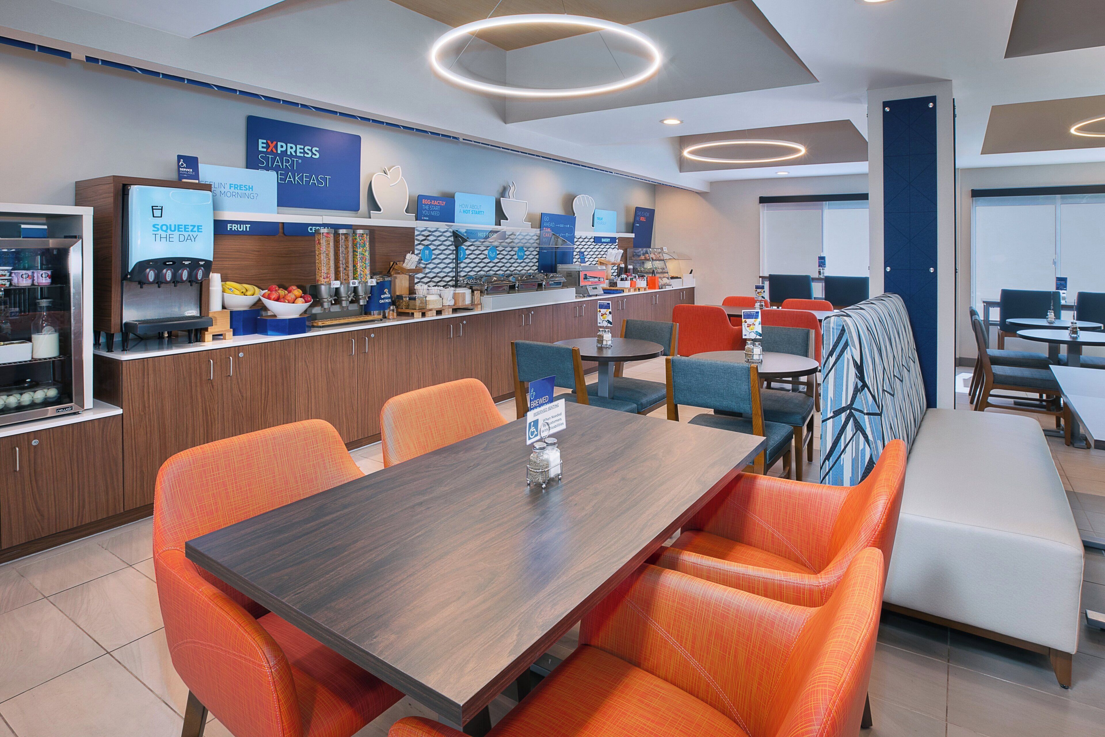 A modern cafe with a breakfast bar, seating area, and a variety of food and drink options.