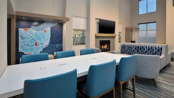 Ein moderner Konferenzraum mit einem langen Tisch, blauen Stühlen, einem Kamin und einem an der Wand montierten Fernseher.