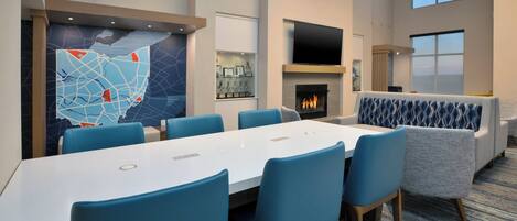 Una sala de conferencias moderna con una mesa larga, sillas azules, una chimenea y un televisor montado en la pared.