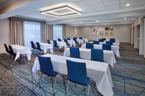 A conference room with rows of tables and chairs, a carpeted floor, and a ceiling with recessed lighting.