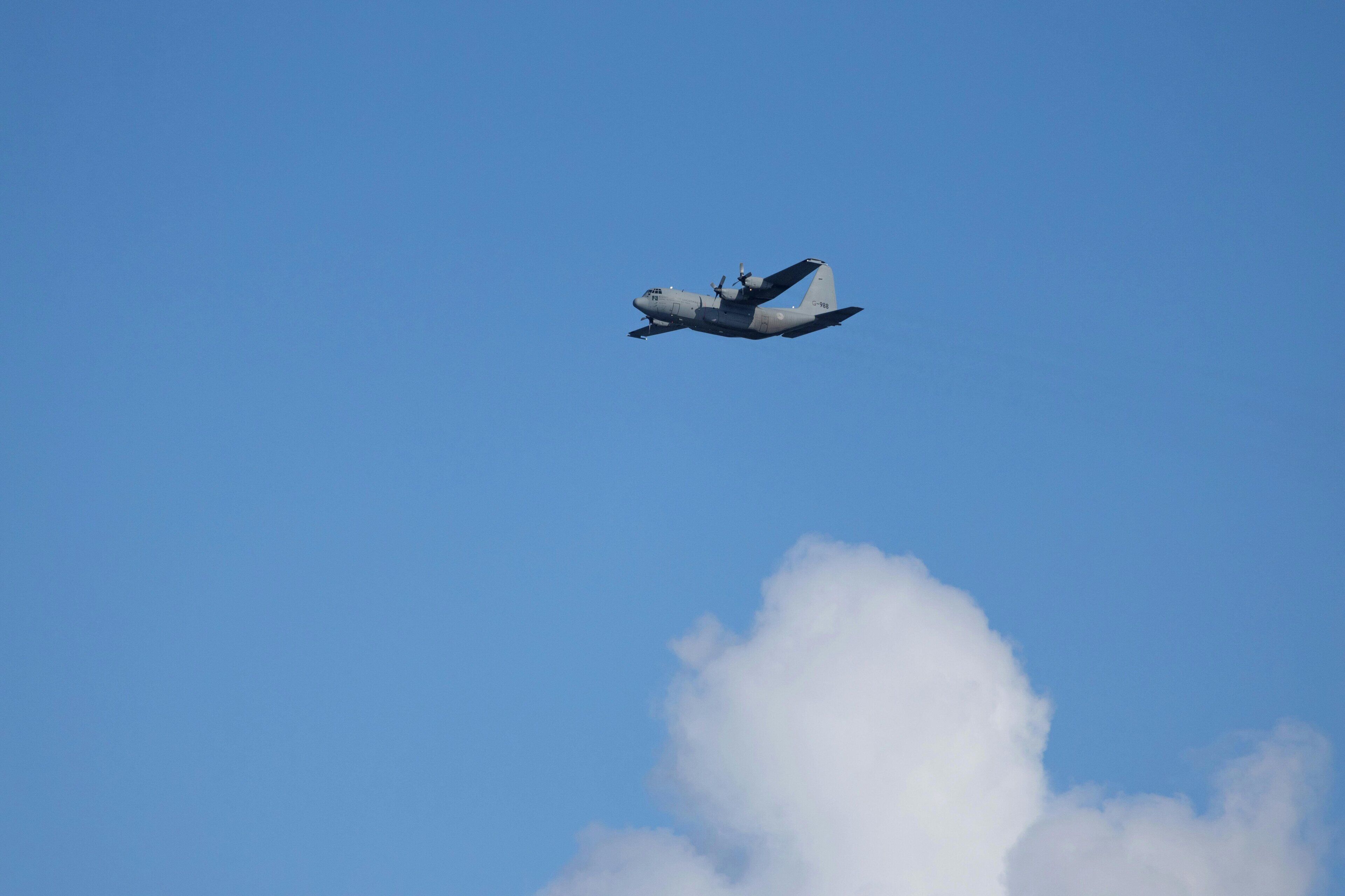 A large aircraft flying in a clear blue sky with a cloud below.