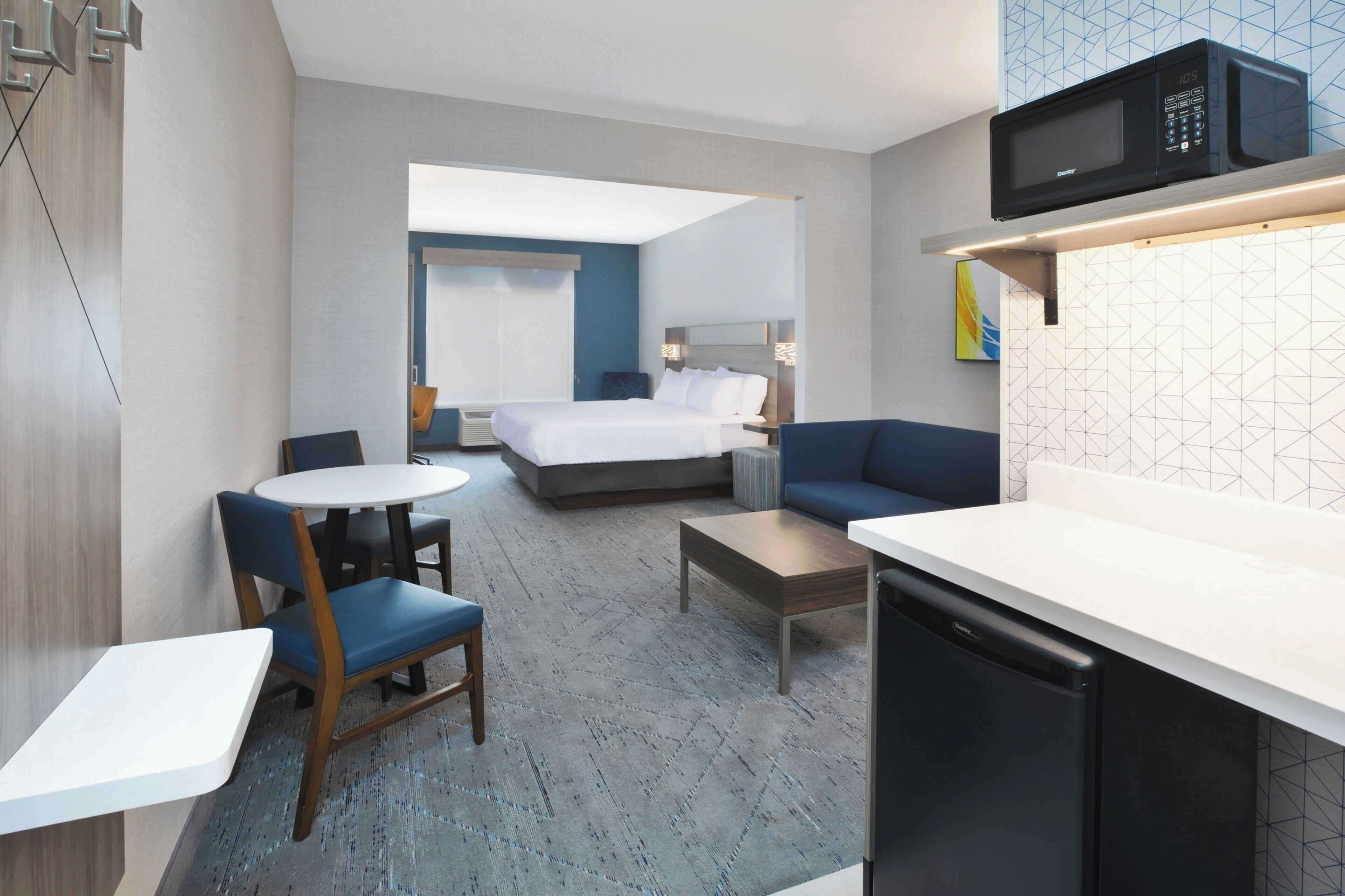 A hotel room with a bed, a sofa, a dining table, a kitchen area, and a microwave.