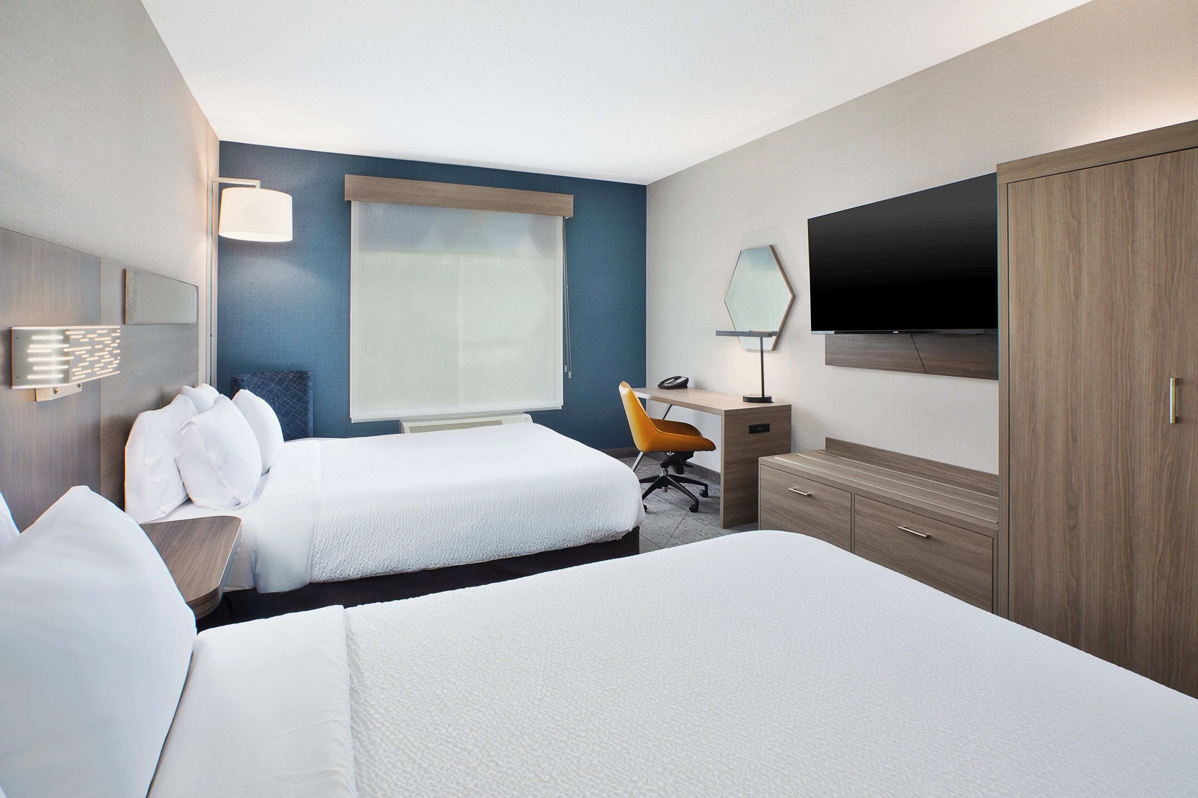 A hotel room with two beds, a desk, a chair, a TV, and a wardrobe.
