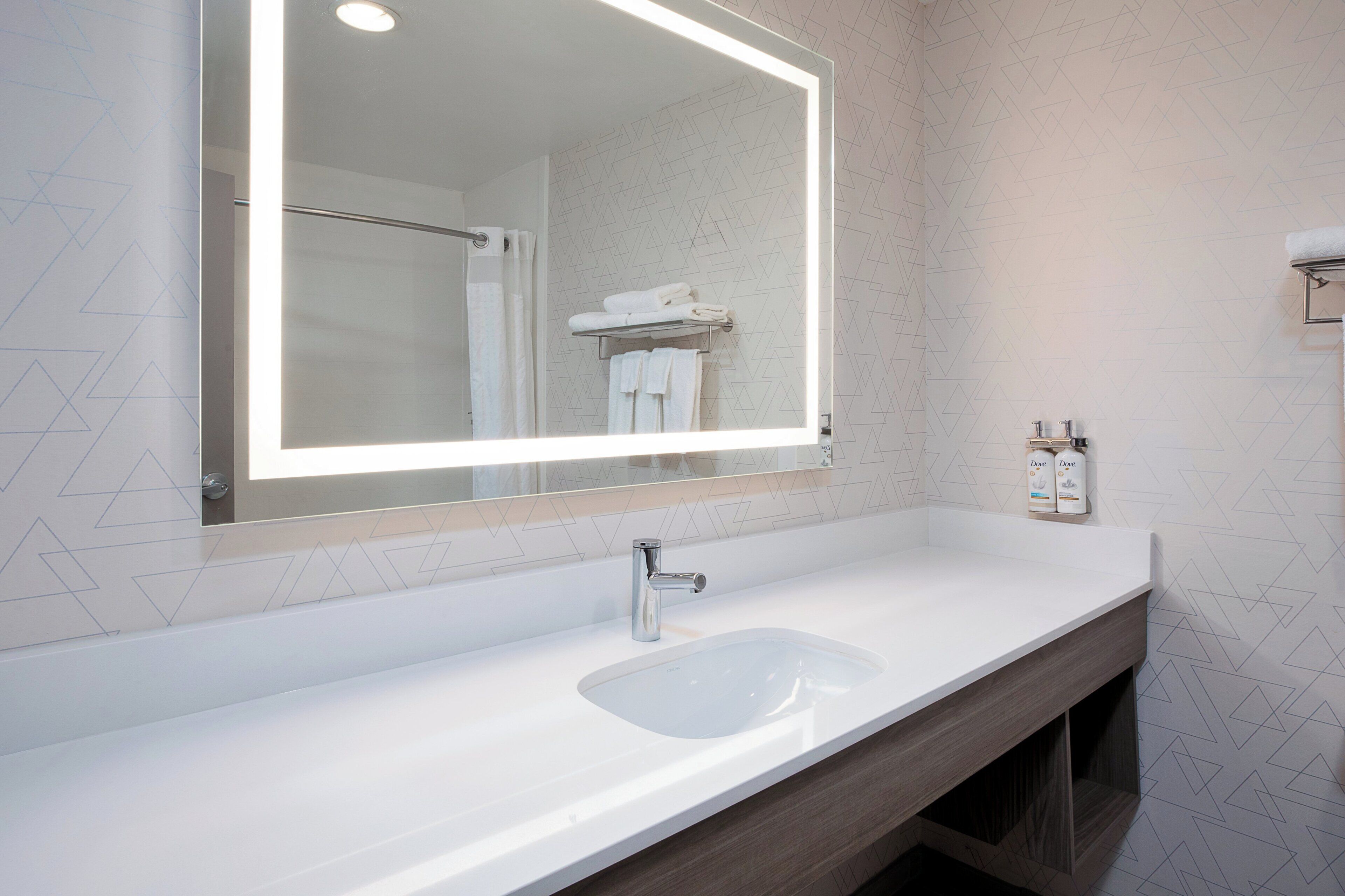 A bathroom with a large mirror, a sink, and a towel rack.
