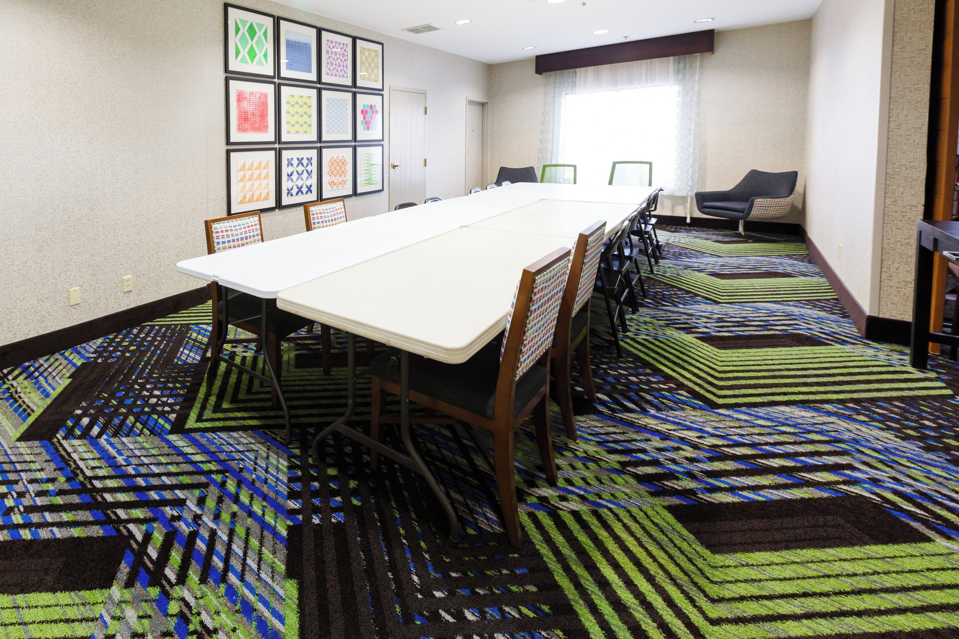 A conference room with a long table, chairs, a carpeted floor, and framed pictures on the wall.