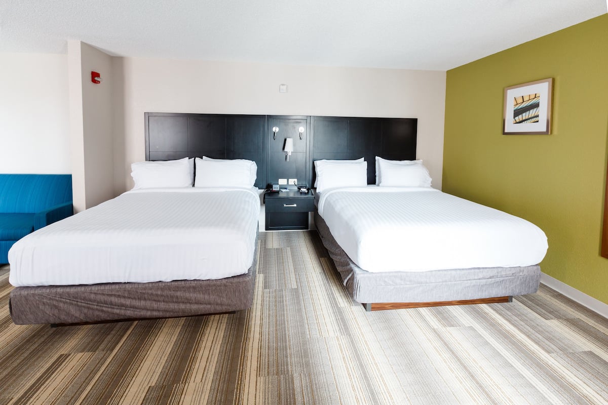 A hotel room with two beds, a nightstand, a lamp, and a framed picture on the wall.