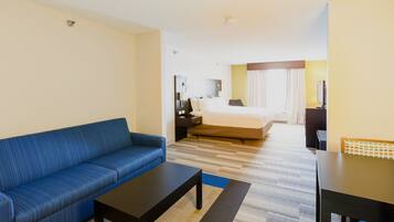 A hotel room with a blue sofa, a bed with a white duvet, a desk with a chair, and a television.