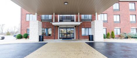 A building entrance with a covered walkway, brick facade, and large windows.