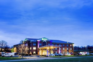 Un hotel Holiday Inn Express con fachada de ladrillo, varios espacios de estacionamiento y una entrada bien iluminada.