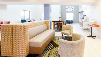 Un moderno vestíbulo de hotel con un sofá, sillones, una zona de comedor y una kitchenette.