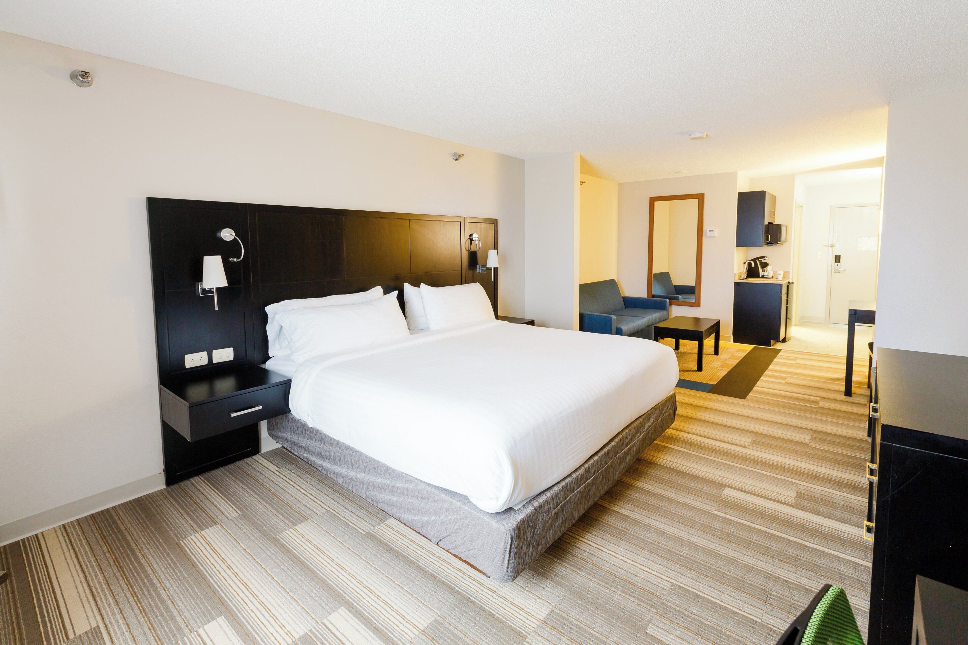 Une chambre d’hôtel avec un grand lit, des tables de chevet, un bureau, une chaise, un miroir et une armoire.