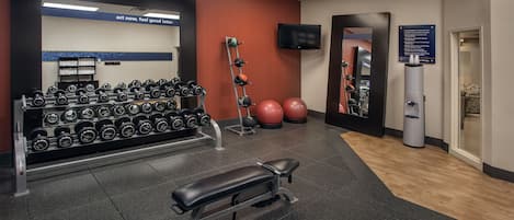 A gym with weightlifting equipment, a bench, and exercise balls.