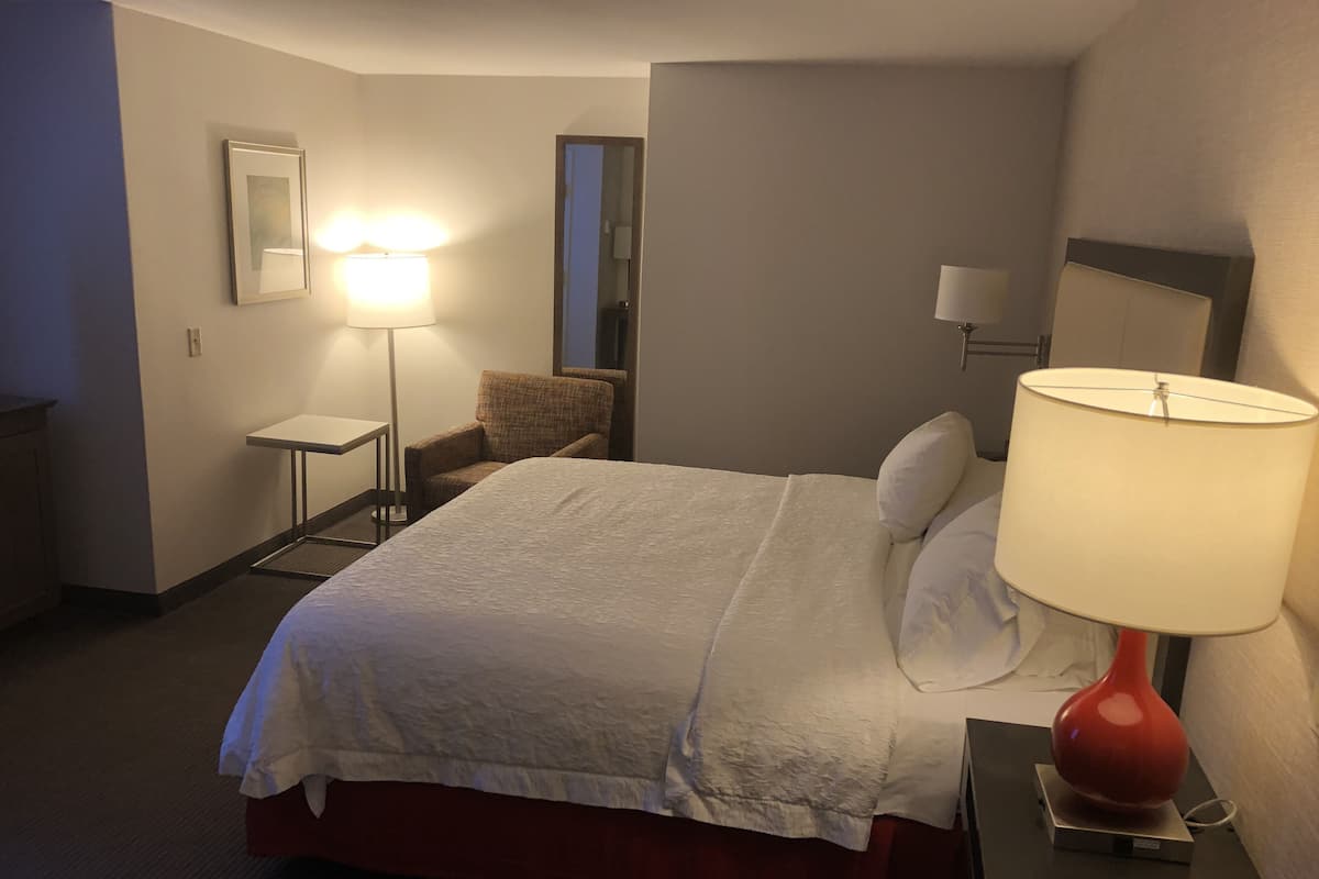 A hotel room with a bed, a desk, a chair, a lamp, and a mirror.
