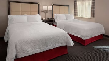 A hotel room with two beds, each with a red base and white bedding. There is a nightstand with a lamp and a phone between the beds.