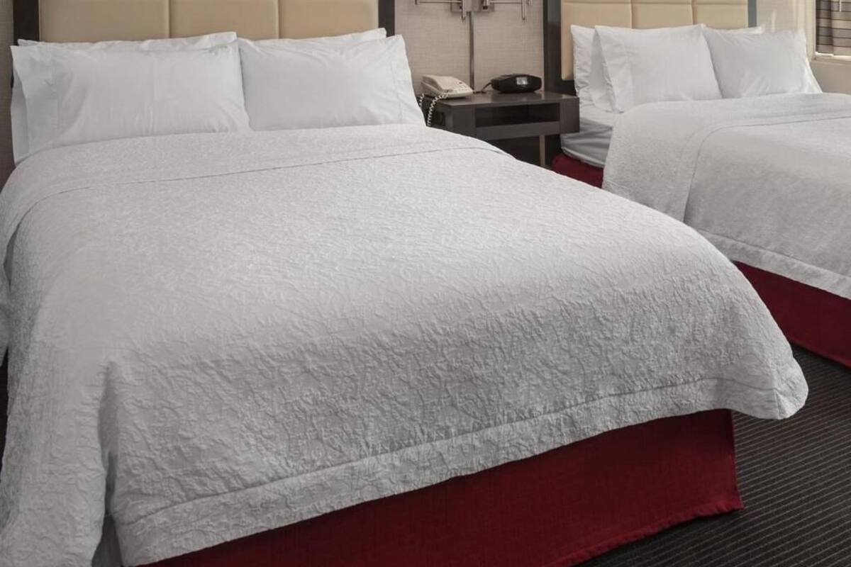 Two beds with white bedding and red bed skirts in a hotel room.