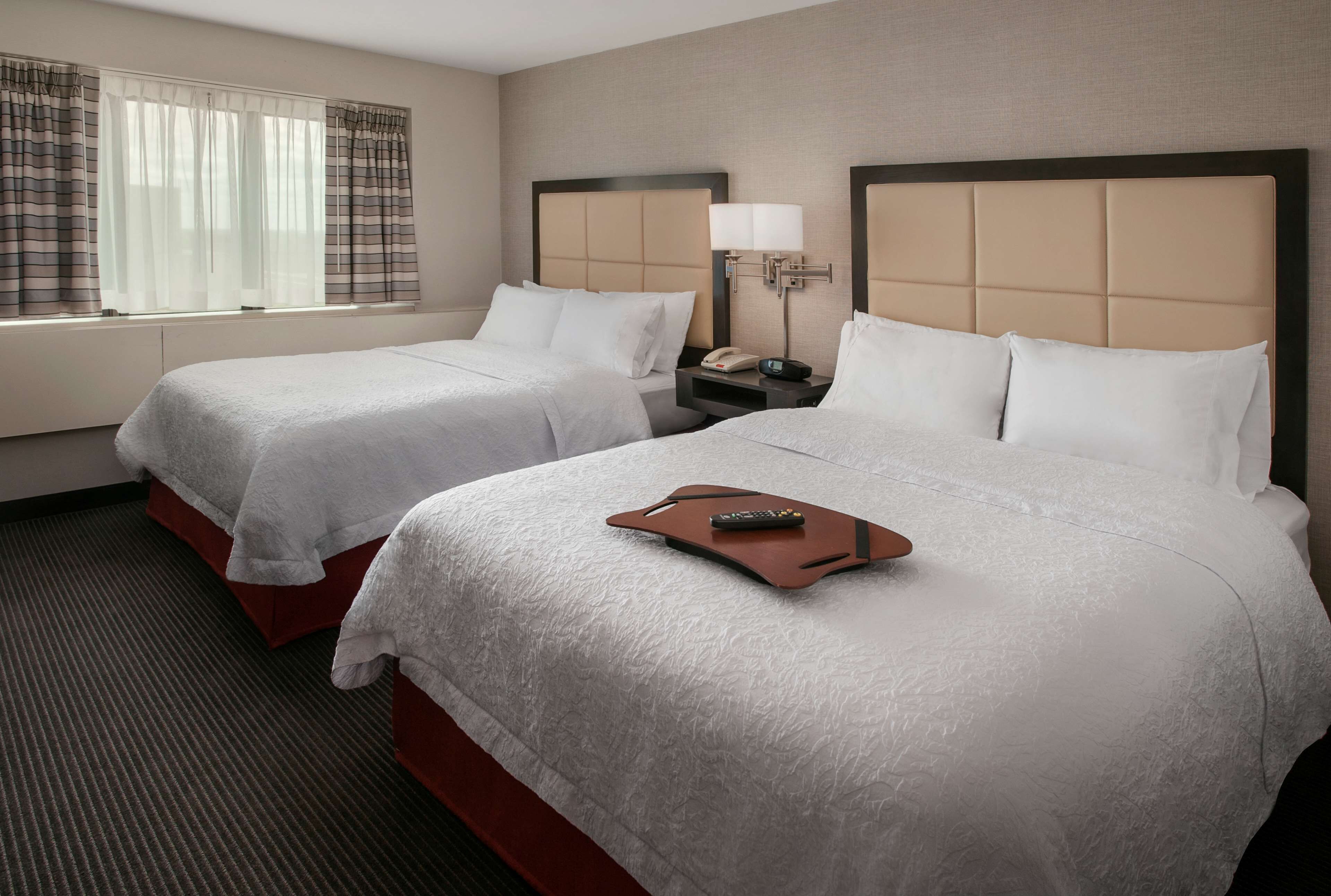 A hotel room with two beds, a nightstand with a lamp, and a window with curtains.