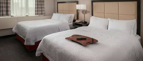 A hotel room with two beds, a nightstand with a lamp, and a window with curtains.