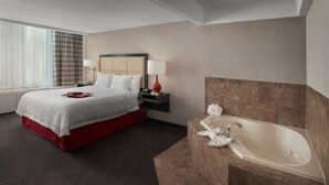 Une chambre d’hôtel comprenant un lit, une table de chevet, une lampe, une salle de bain avec baignoire et une fenêtre avec des rideaux.