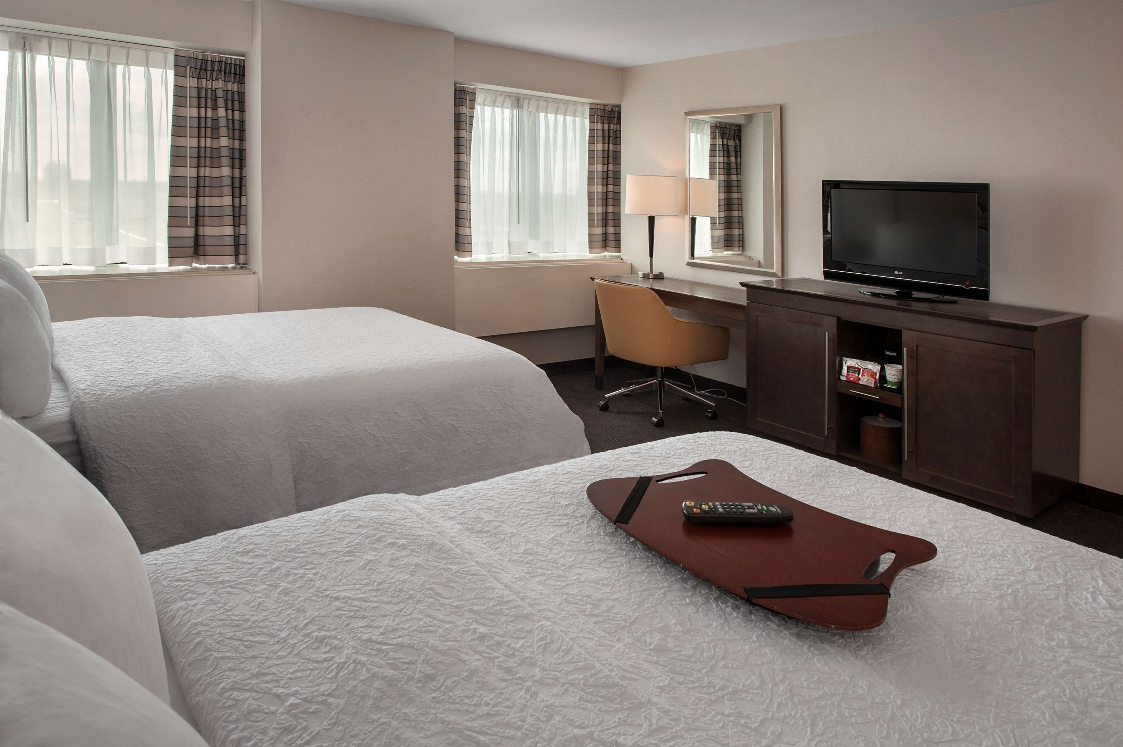 A hotel room with two beds, a desk with a chair, a television, and a remote control on a tray.