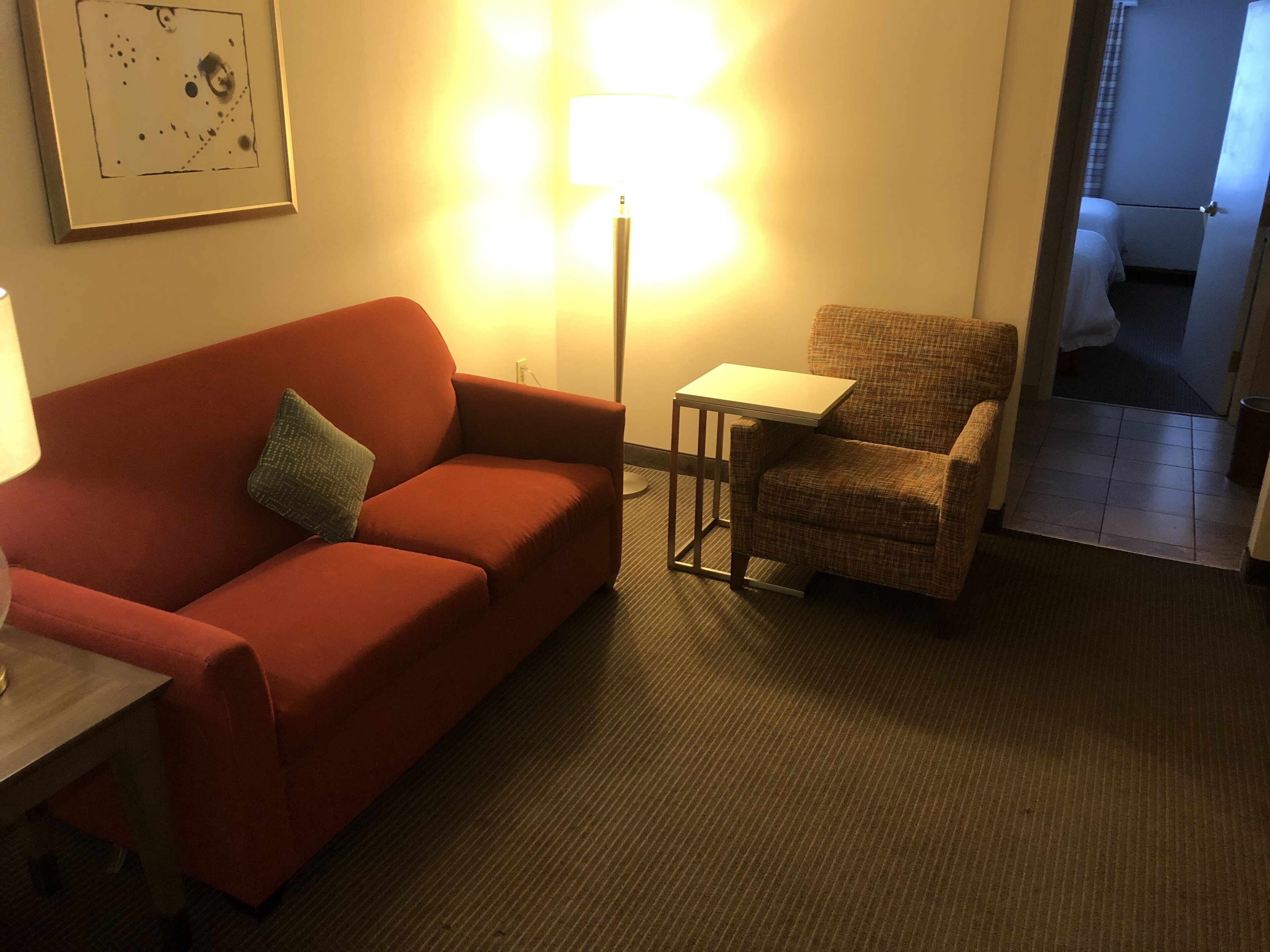 Ein Zimmer mit einem roten Sofa, einem kleinen Tisch, einer Lampe und einem karierten Sessel.