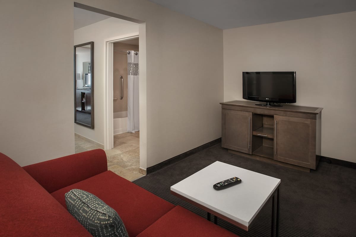 A hotel room with a red sofa, a white coffee table, a television on a wooden cabinet, and a mirror on the wall.