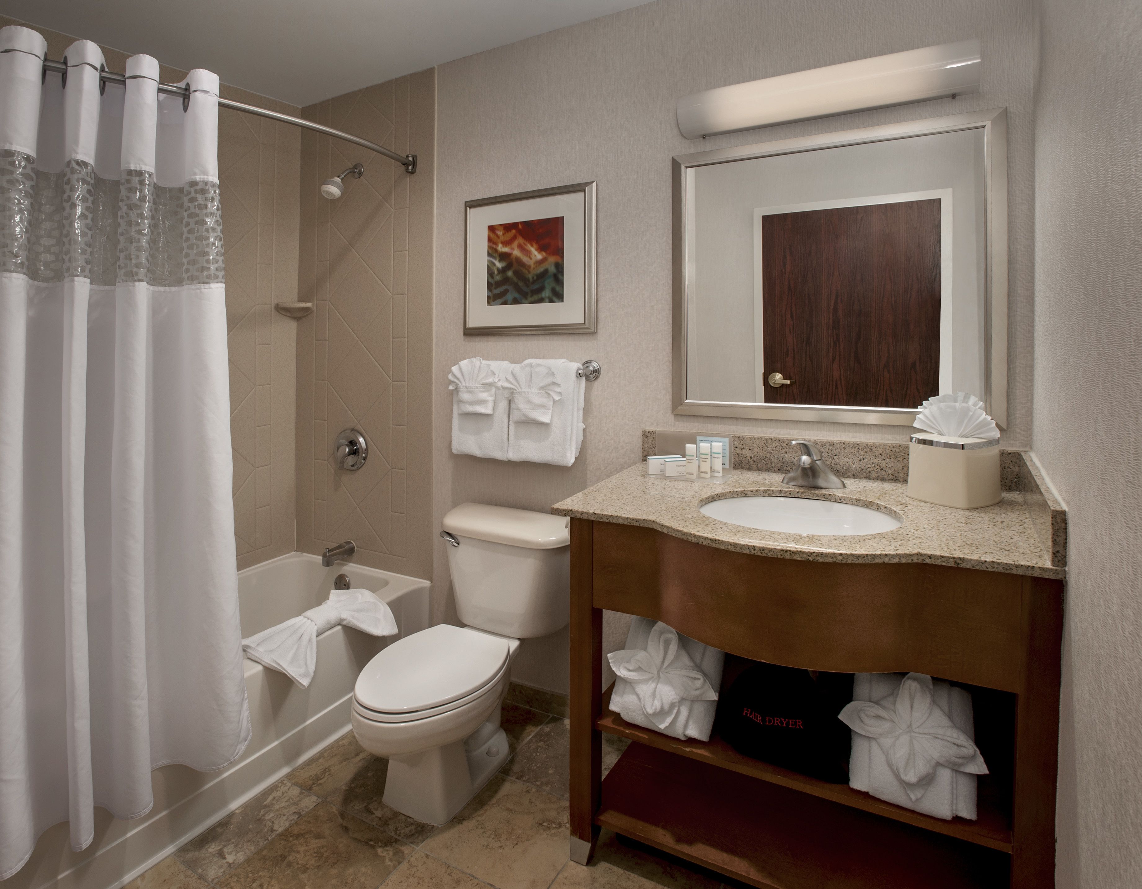 A bathroom with a shower, toilet, sink, and a mirror.