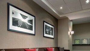 Un espace détente moderne avec un canapé marron, des coussins rouges et gris, et deux petites tables d’appoint en bois.