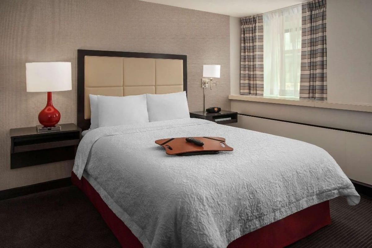 A hotel room with a bed, two bedside tables, a lamp, and a window with curtains.