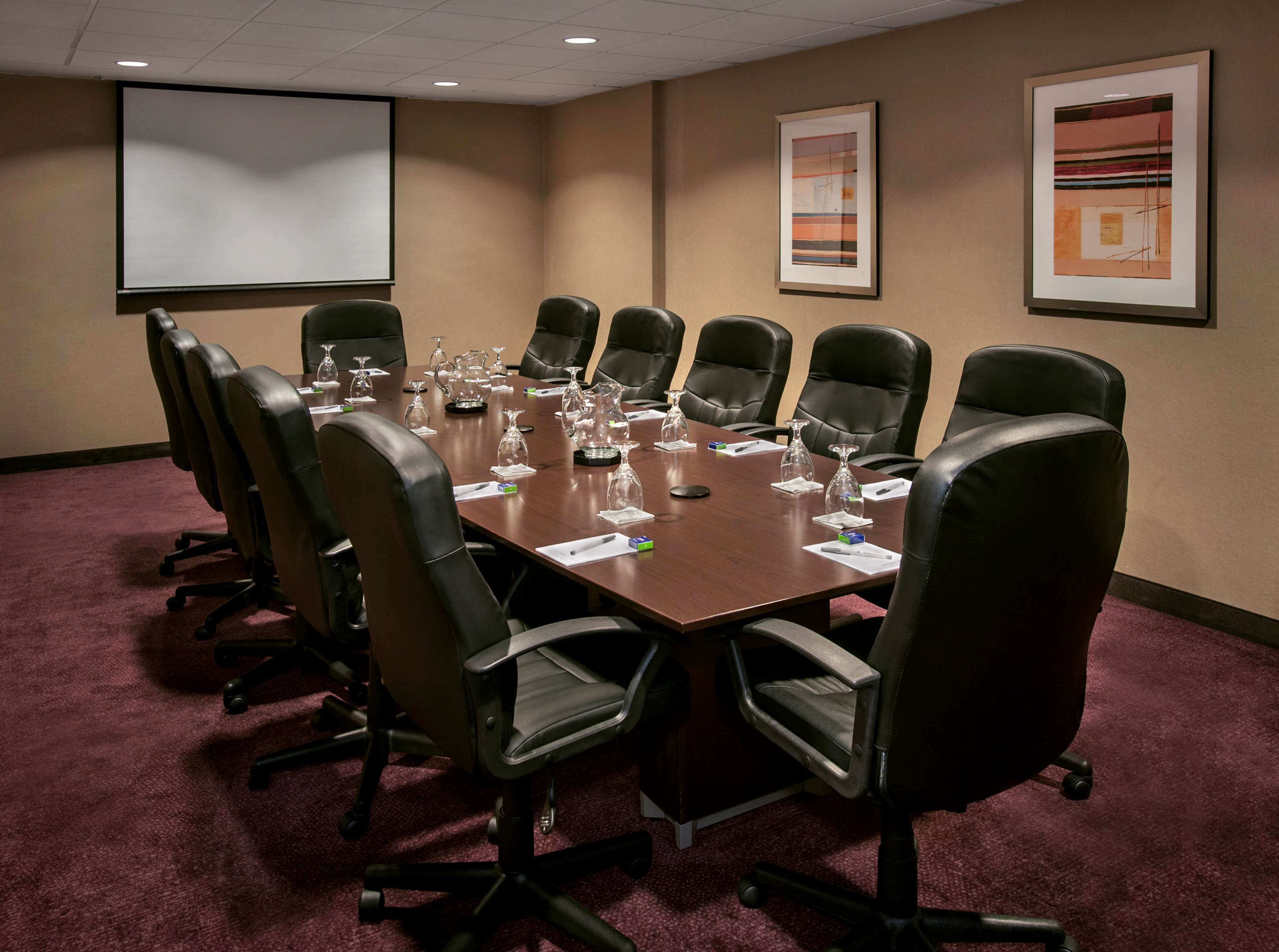 A conference room with a long table, multiple chairs, and a projector screen.