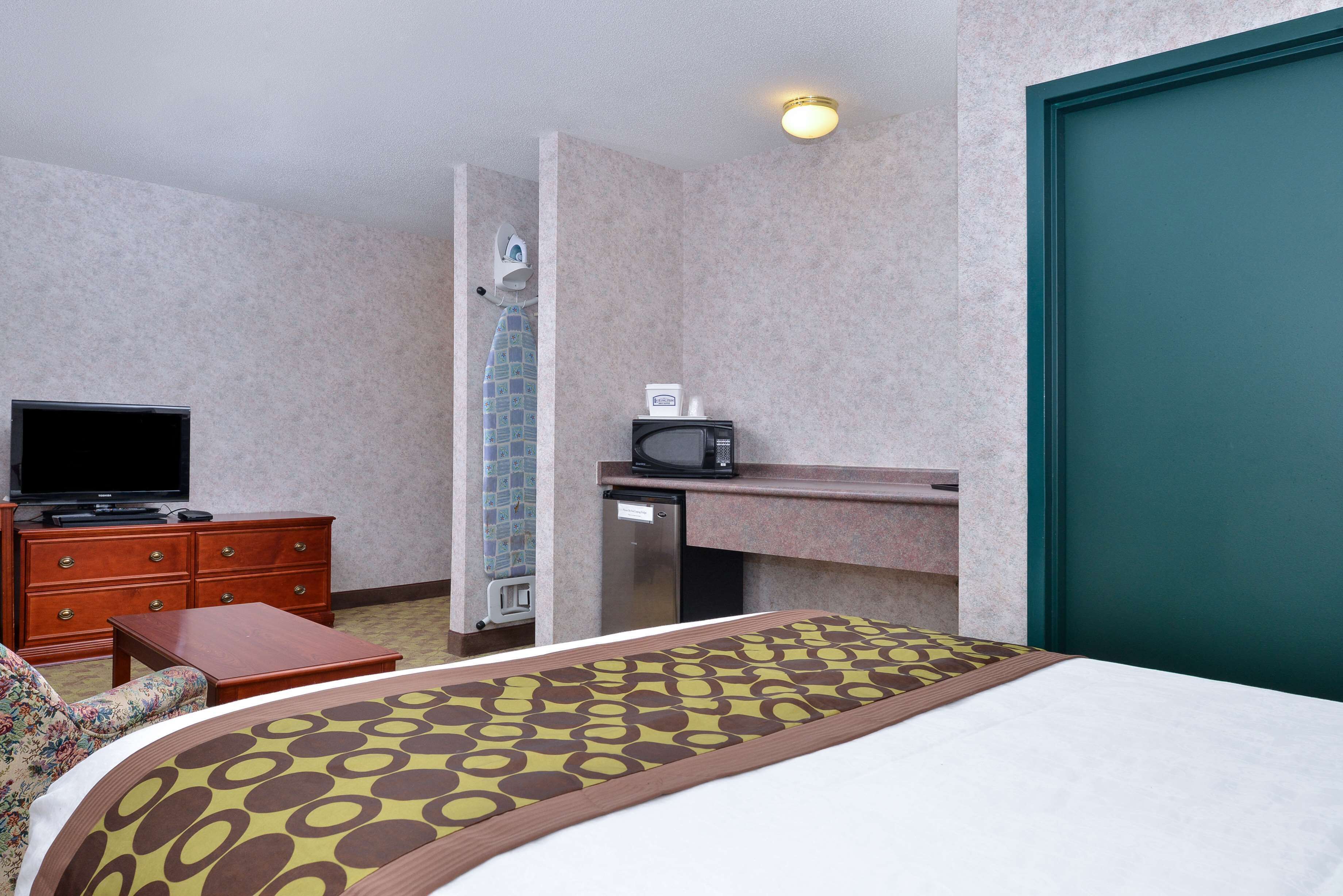 A hotel room with a bed, a television, a microwave, a small desk, and a bathroom with a shower.