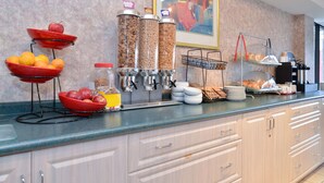 A breakfast bar with fruit bowls, a coffee station, and a bread rack. - Lexington Inn & Suites Windsor (Windsor)