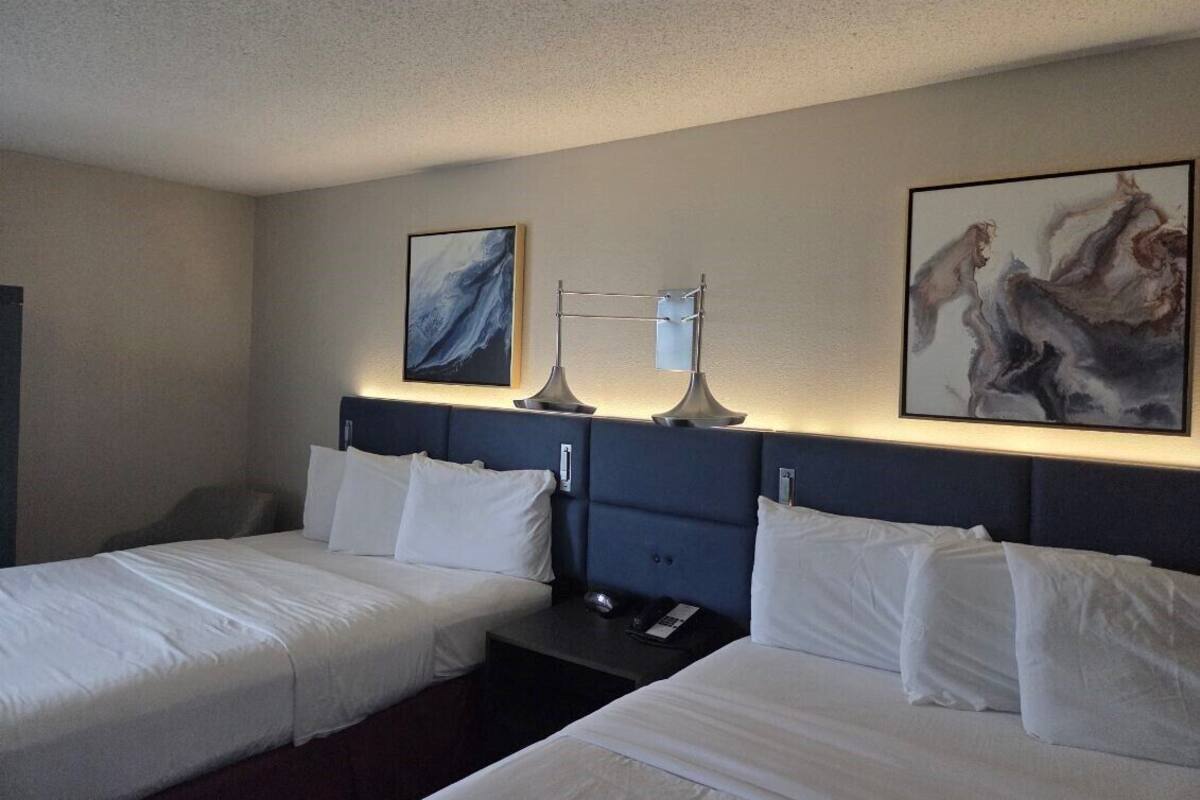 A hotel room with two beds, a nightstand, a lamp, and artwork on the walls.