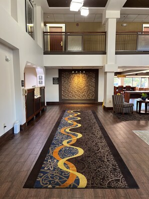 A hotel lobby with a central decorative wall, a reception desk, and a seating area with tables and chairs.