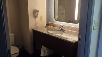 Un baño con inodoro blanco, un lavabo con espejo y un secador de pelo en la pared.
