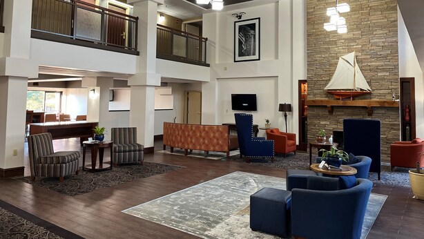 A spacious lobby with a high ceiling, a wooden staircase, a fireplace with a sailboat decoration, and a television mounted on the wall. - Hamilton Inn Bessemer, AL - Birmingham (Bessemer)