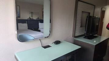 A hotel room with a bed, a desk with a computer, a chair, a television, and a mirror.