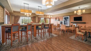 A spacious dining area with a long wooden table and chairs, overhead pendant lighting, and a television mounted on the wall. - Hamilton Inn Bessemer, AL - Birmingham (Bessemer)