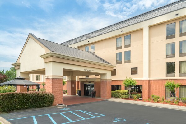A hotel entrance with a covered area, a parking lot with handicapped spaces, and a clear sky.