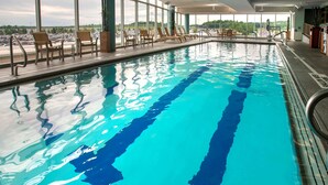 An indoor swimming pool with clear blue water, large windows offering views of a parking lot and greenery, and sun loungers along the poolside. - Hyatt Regency Pittsburgh International Airport (Pittsburgh)