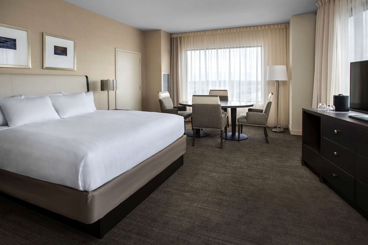 A hotel room with a large bed, a desk, two chairs, a television, and a lamp.