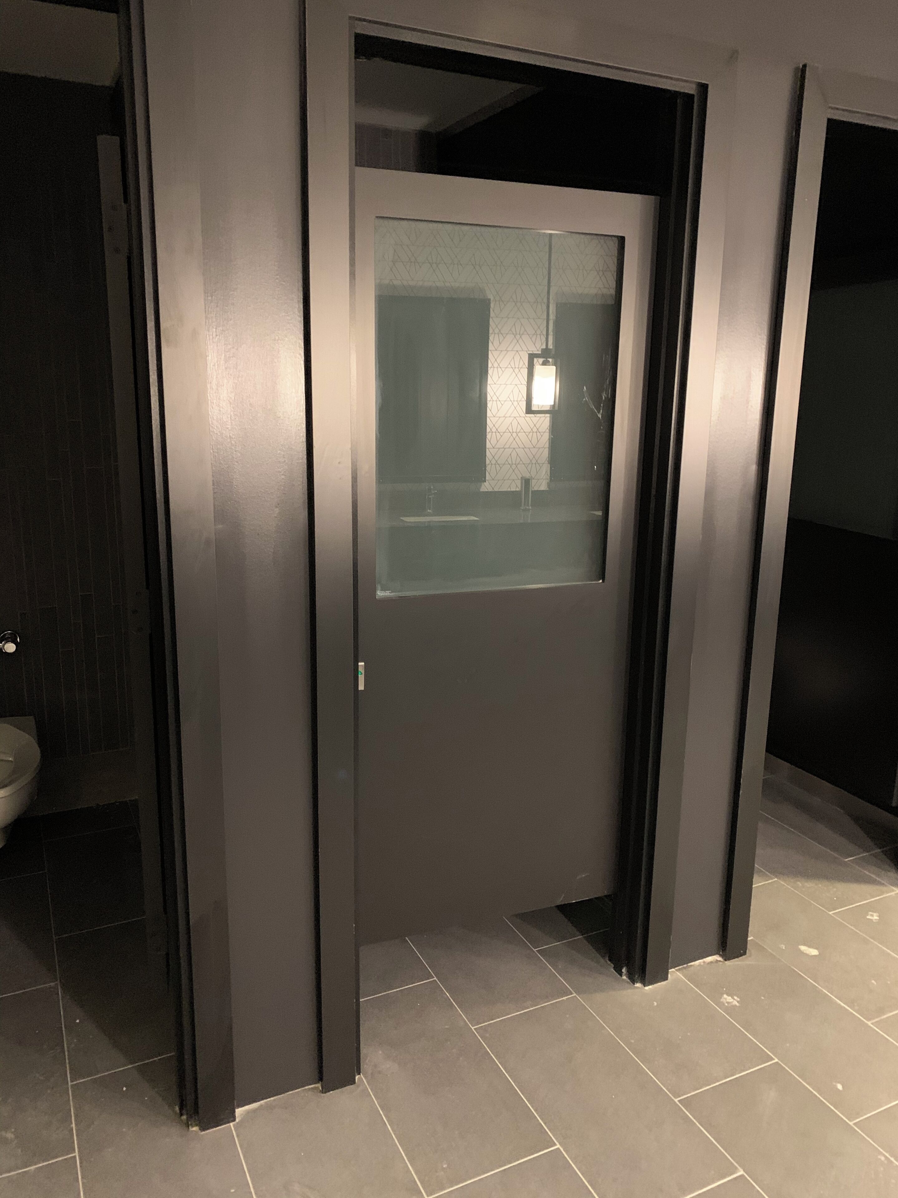Un baño moderno con una puerta oscura, un panel de vidrio y un inodoro a la vista.