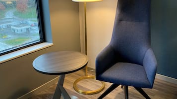 A modern room with a round table, a blue armchair, a floor lamp, and a view of a parking lot through a window.