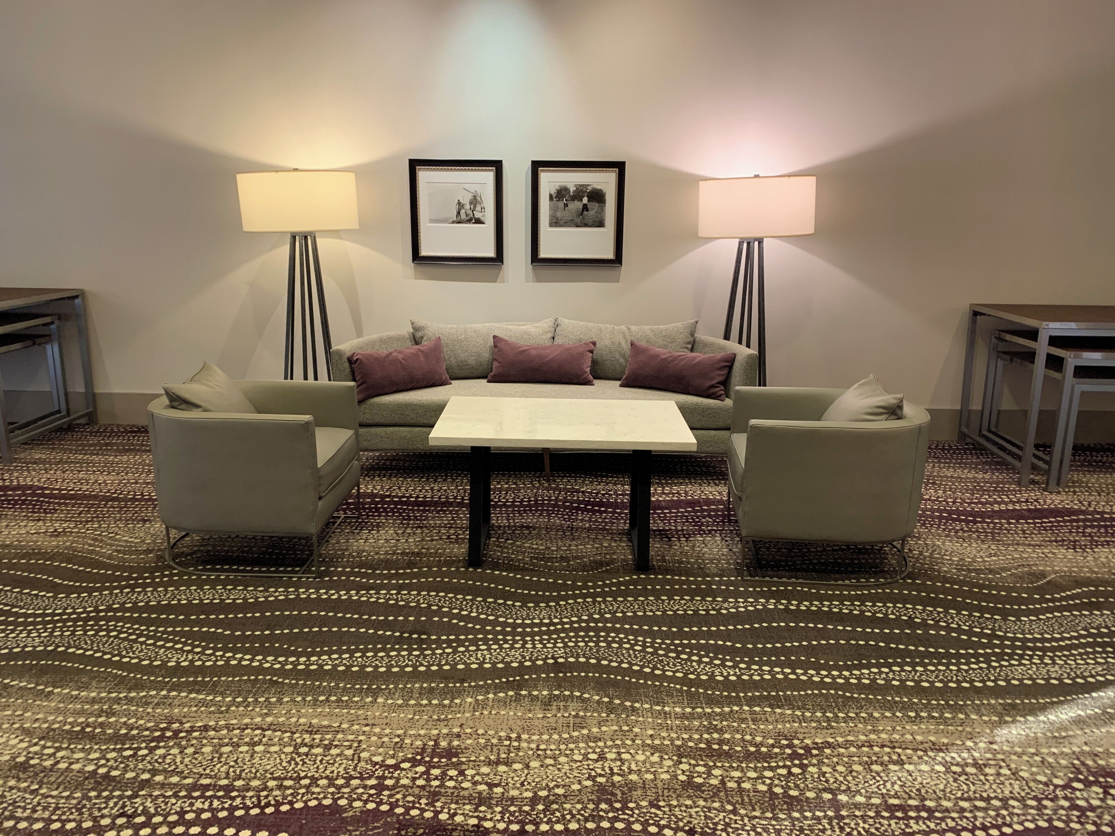 A living room with a sofa, two armchairs, a coffee table, and two lamps. There are two framed pictures on the wall.