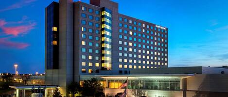A multi-story hotel with a modern design, featuring a prominent entrance with glass doors and a flag display.