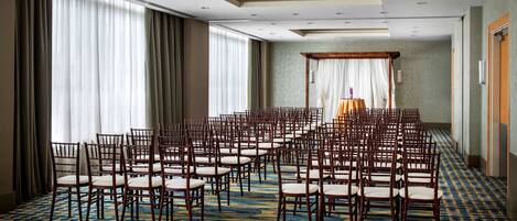 A conference room with rows of wooden chairs and a stage with a table and drapes.