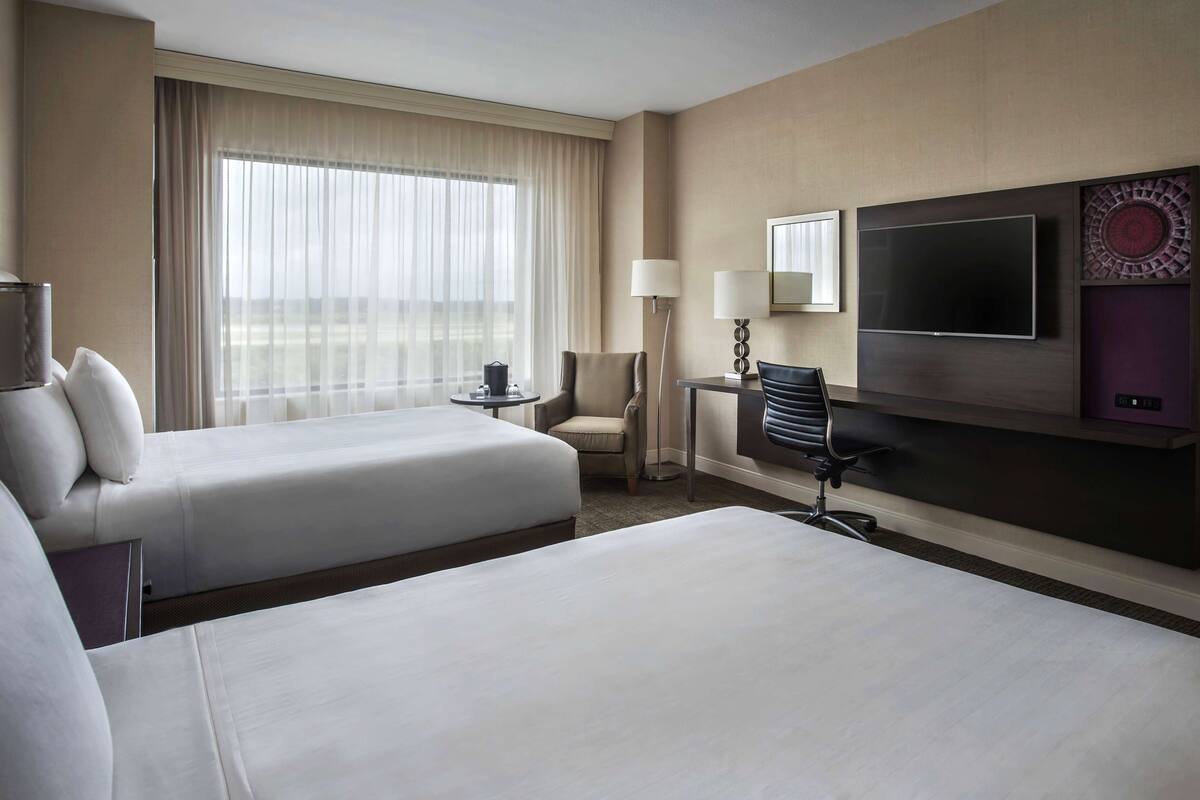 A hotel room with two beds, a TV, a desk, a chair, and a window with curtains.