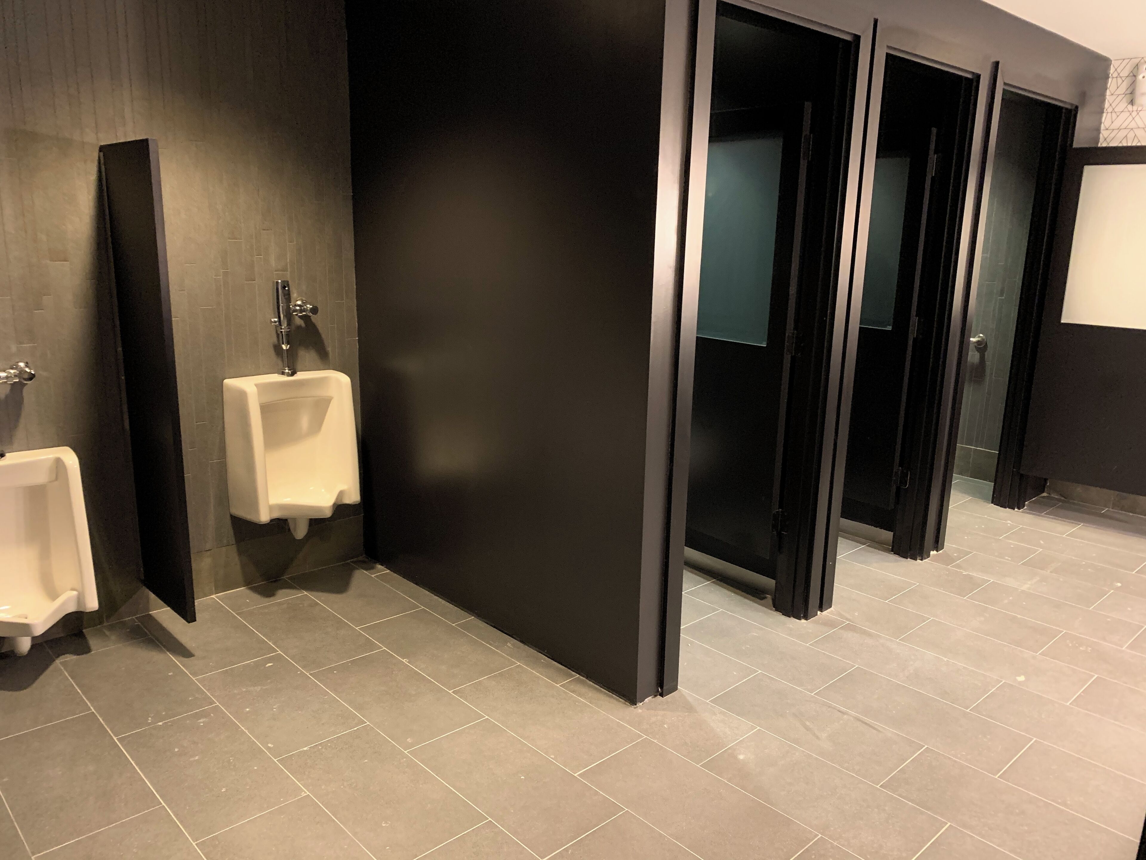 Uma casa de banho moderna com dois sanitários masculinos, um espelho e uma divisória de parede preta.